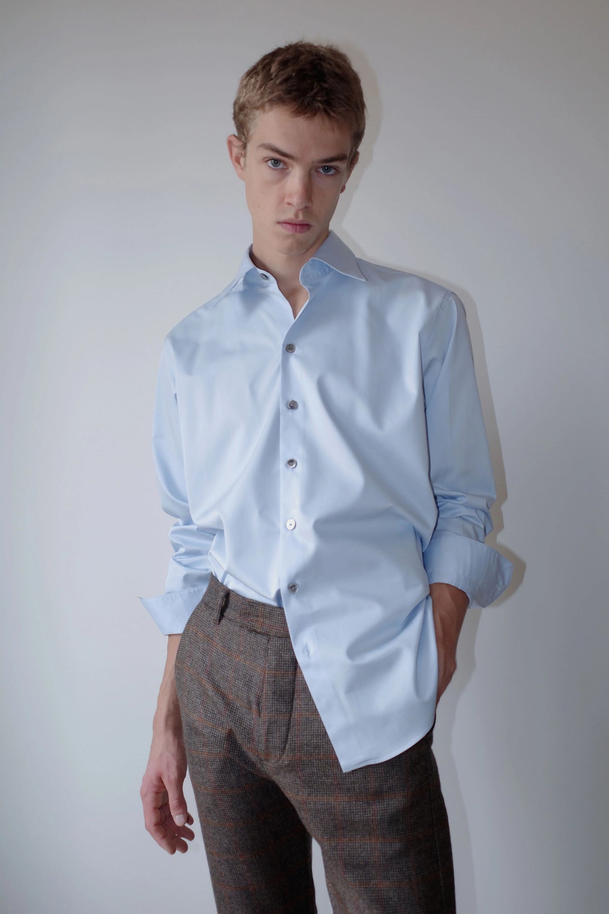CAMISAS MANOLO(カミサス マノロ)Normal Shirt Light Blue スタイリング画像。ライトブルーの長袖シャツにチェック柄のトラウザーを合わせた着用スタイル。袖をまくり、裾を一部タックインしたコーディネート。