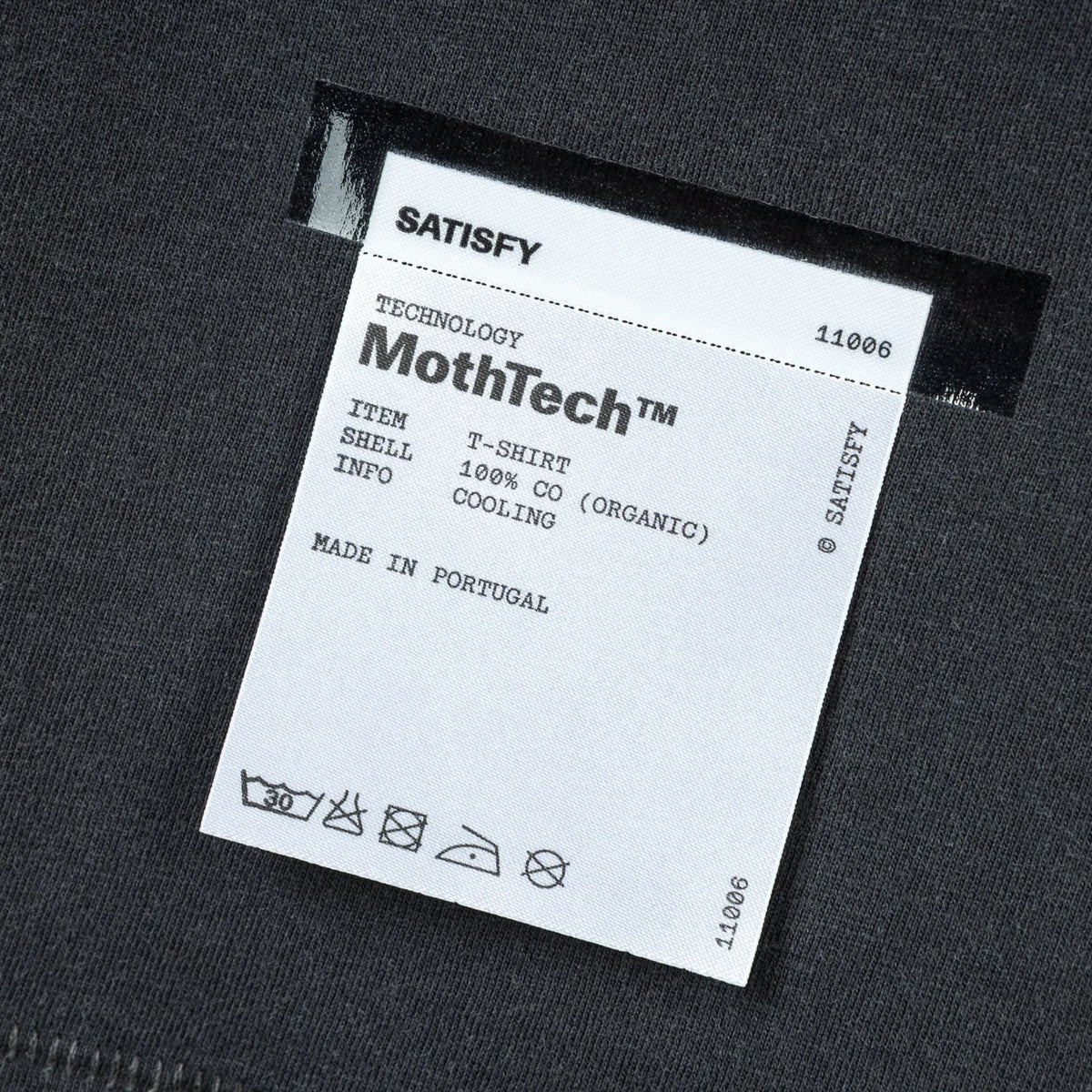 SATISFY MothTech™ T-Shirt Aged Black AirBrush Glitterのケアラベル。外側に配置された取り外し可能なブランドラベルのディテール。