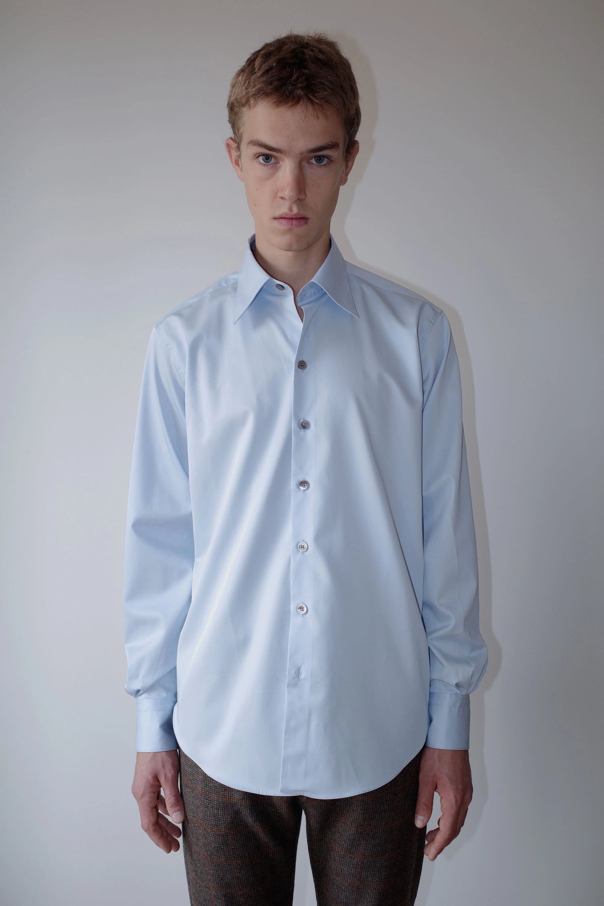 CAMISAS MANOLO（カミサス マノロ）Normal Shirt Light Blue 正面着用画像。淡いライトブルーのコットンツイル生地を使用した長袖シャツ。リラックス感のあるシルエットとラウンドヘムが特徴。