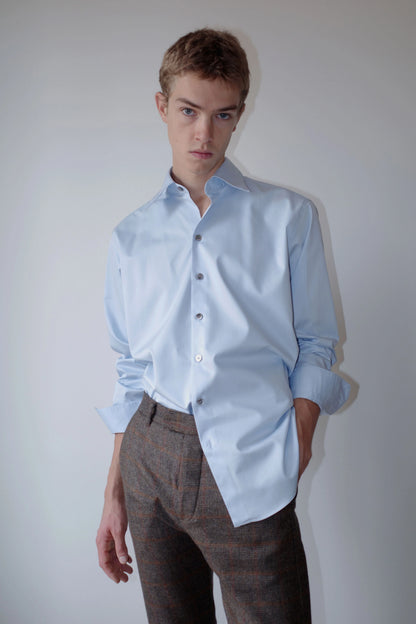 CAMISAS MANOLO（カミサス マノロ）Normal Shirt Light Blue スタイリング画像。ライトブルーの長袖シャツにチェック柄のトラウザーを合わせた着用スタイル。袖をまくり、裾を一部タックインしたコーディネート。