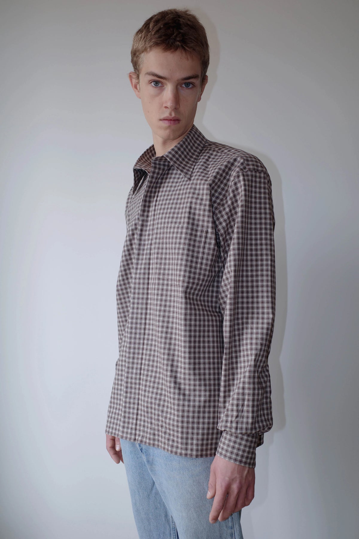 CAMISAS MANOLO（カミサス マノロ）Campo Shirt Brown/Camel Checksの斜め前からの着用画像。ブラウンとキャメルのチェック柄が特徴的な長袖シャツ。自然な生地のドレープと短めの着丈、襟元のディテールが確認できる。