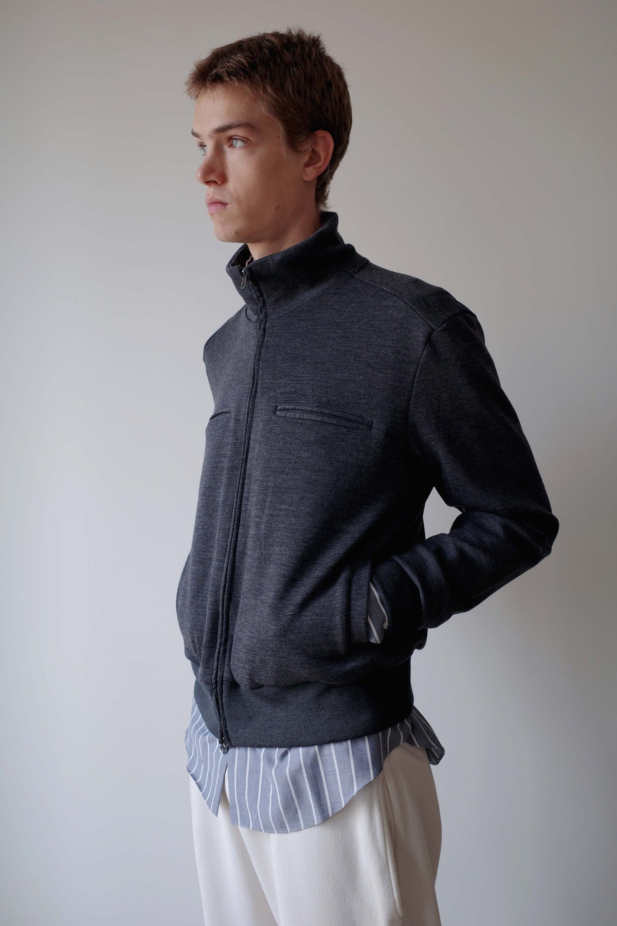 CAMISAS MANOLO（カミサス マノロ）Jersey CM Jacket Greyの斜め横からの着用画像。グレーのウールジャージージャケットで、スタンドカラーとすっきりとしたシルエットが特徴。サイドポケットに手を入れた着用スタイル。