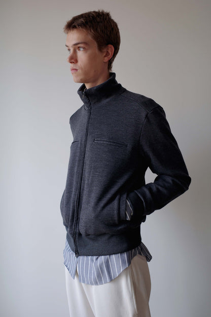 CAMISAS MANOLO（カミサス マノロ）Jersey CM Jacket Greyの斜め横からの着用画像。グレーのウールジャージージャケットで、スタンドカラーとすっきりとしたシルエットが特徴。サイドポケットに手を入れた着用スタイル。