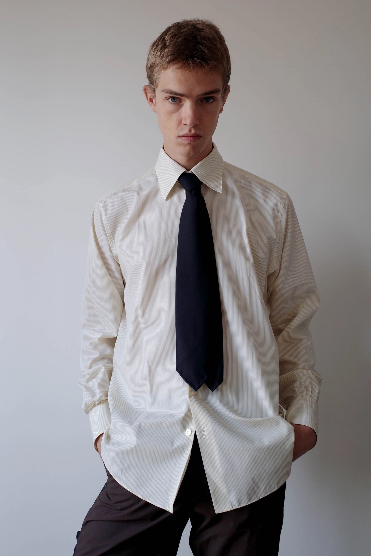 CAMISAS MANOLO（カミサス マノロ）Normal Shirt Pale Yellow Black Stripesのスタイリング画像。淡いイエローのストライプシャツにネイビーのネクタイとダークカラーのトラウザーを合わせた着用スタイル。リラックスしたシルエットとクラシックな襟元が特徴。