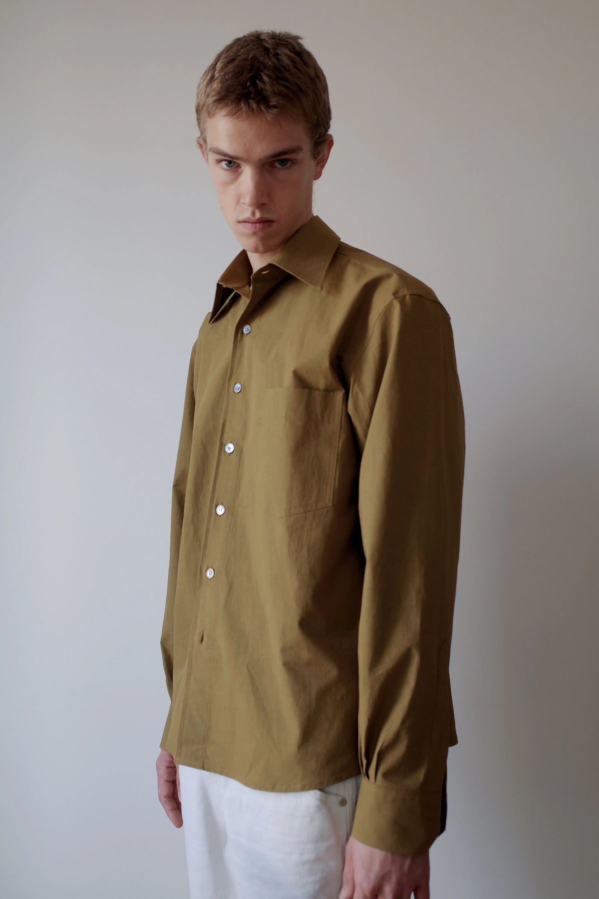 CAMISAS MANOLO（カミサス マノロ）Sobrecamisa Shirt Oliveの斜め前からの着用画像。オリーブカラーのコットンシャツで、ゆとりのある身幅と自然な生地のドレープ、胸元のポケットや襟元のディテールが確認できる。