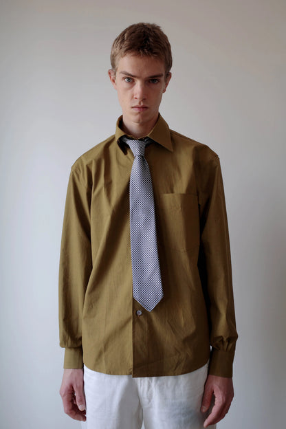 CAMISAS MANOLO（カミサス マノロ）Sobrecamisa Shirt Oliveのスタイリング画像。オリーブカラーの長袖シャツに柄物のネクタイとホワイトのトラウザーを合わせた着用スタイル。オーバーサイズのシルエットと落ち着いた色合いが特徴。