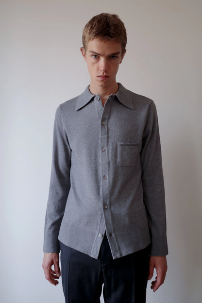CAMISAS MANOLO（カミサス マノロ）Knitted Shirt Light Greyの正面着用画像。ライトグレーのコットン×メリノウール素材を使用した長袖ニットシャツ。すっきりとしたシルエットと胸元のパッチポケット、ストレートヘムが特徴。
