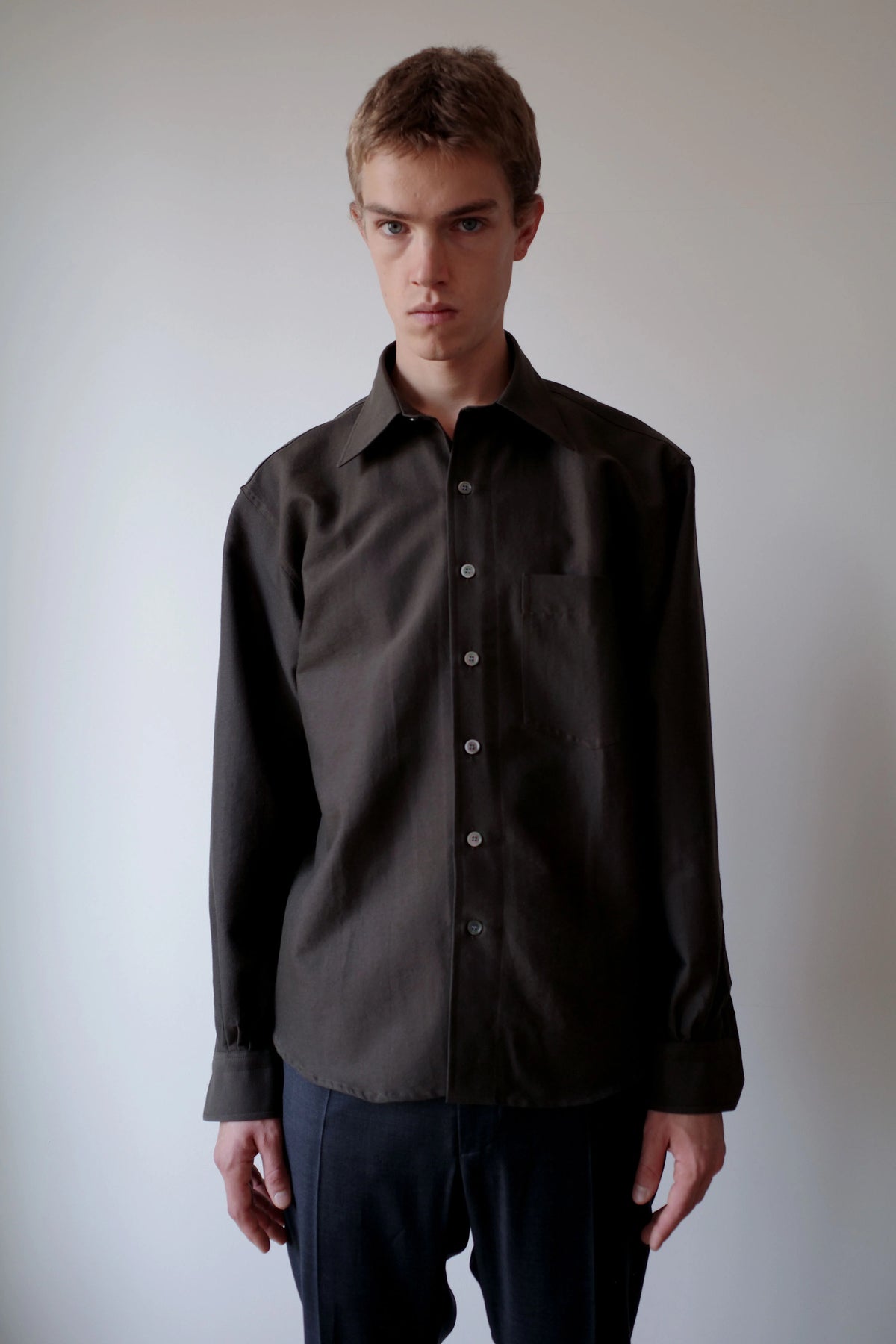 CAMISAS MANOLO（カミサス マノロ）Sobrecamisa Shirt Greenの正面着用画像。落ち着いたダークグリーンの長袖シャツ。ゆとりのあるシルエットと胸元のシングルポケット、緩やかなラウンドヘムが特徴。