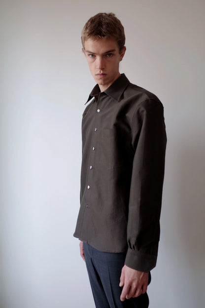 CAMISAS MANOLO（カミサス マノロ）Sobrecamisa Shirt Greenの斜め前からの着用画像。深みのあるグリーンの長袖シャツで、自然な生地のドレープとゆとりのある身幅、襟元や袖口のディテールが確認できる。