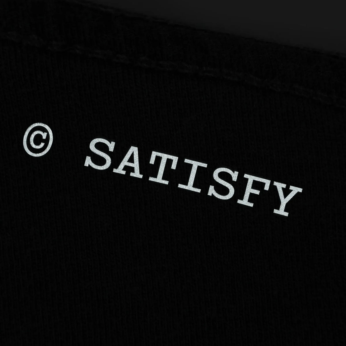 SATISFY MothTech™ T-Shirt Aged Black AirBrush Glitterのバックディテール。背面に配置された©SATISFYリフレクターロゴ。